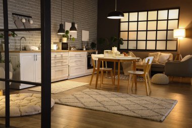 Parlayan lambaları, yemek masası, beyaz tezgahları ve akşamları gri kanepesi olan modern mutfağın içi.