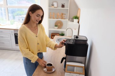 Mutfakta kahve makinesi kullanan güzel genç bir kadın.