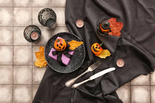 Halloween table setting with burning candles and gift box on color tile background