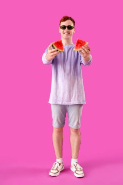 Mor arka planda taze karpuz dilimleri olan güneş gözlüklü genç kızıl adam.
