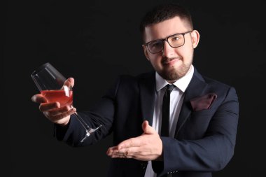 Genç şarap garsonu siyah arka planda bir kadeh şarap gösteriyor.