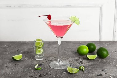 Bir bardak Cosmopolitan kokteyli, gri masada kiraz ve limon.