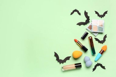Yeşil arka planda Cadılar Bayramı dekoru olan farklı dekoratif kozmetik ürünleri ve rujlar.