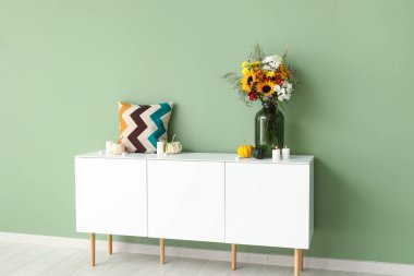 Yeşil duvarın yanında sonbahar çiçekleri olan beyaz büfe.