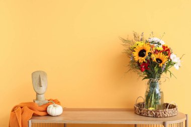 Sonbahar çiçekleri, balkabağı ve turuncu duvarın yanında dekoru olan ahşap raf ünitesi.