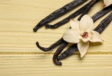Sarı ahşap zemin üzerinde Aromatik vanilya çubukları ve çiçek