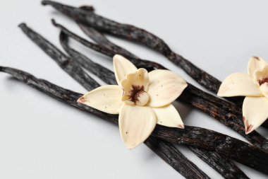 Aromatik vanilya çubukları ve gri arkaplanda çiçekler