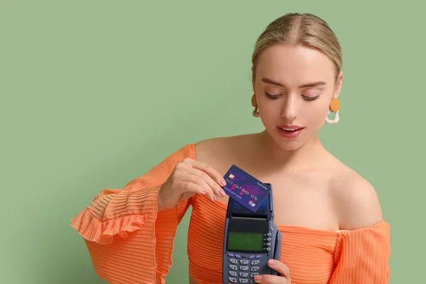 Pretty young woman with credit card and payment terminal on green background