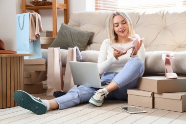 Bilgisayarı, tableti, kutuları ve yeni topuklu ayakkabıları olan genç bir kadın evde online alışveriş yapıyor.