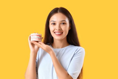 Sarı arka planda çene modeli olan gülümseyen genç Asyalı kadın.