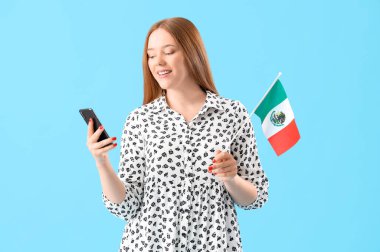 Mavi arka planda Meksika bayrağı ve cep telefonu olan genç bir kadın.
