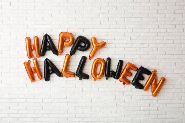 Hafif tuğla duvarda asılı balonlardan yapılmış Mutlu Cadılar Bayramı metni.