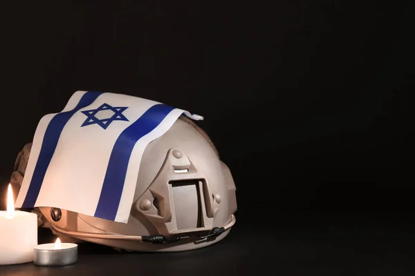 Military helmet with flag of Israel and burning candles on dark background