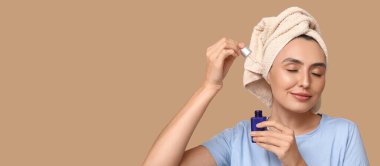 Güzel genç bir kadın bej arka planda kozmetik yağı şişesi tutuyor ve yazı için yeri var.