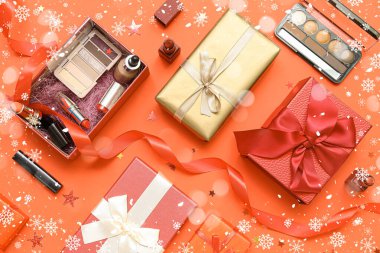 Makyaj ürünleri ve turuncu arka planda Noel dekoru olan hediye kutuları.
