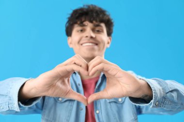 Yakışıklı genç adam elleri açık mavi arka planda kalp yapıyor.