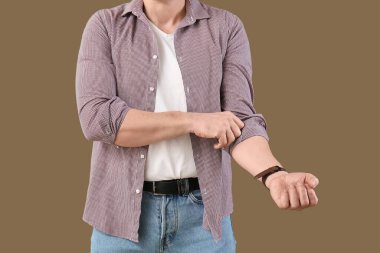 Olgun bir adam yeşil arka planda kolunu kıvırıyor, yakın plan.