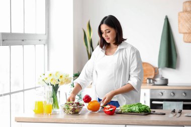 Genç hamile kadın mutfakta sebze salatası yapıyor.