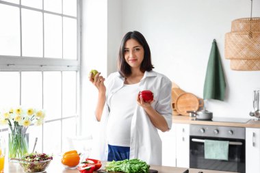 Mutfakta elma ve dolmalık biberli hamile bir kadın.