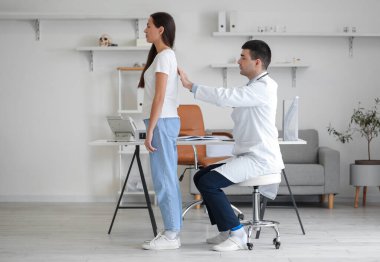 Erkek doktor klinikteki genç kadının duruşunu kontrol ediyor.