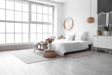 Hafif yatak odasının içinde yumuşak bir bank ve vazoda laleler.