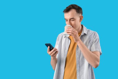 Mavi arka planda bir fincan kahve ve cep telefonuyla mesajlaşan genç adam.
