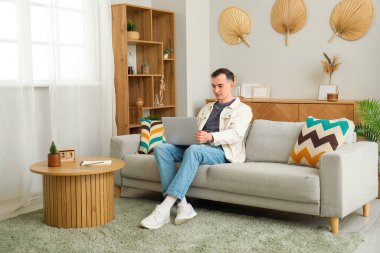 Evde laptopla mesajlaşan genç bir adam.