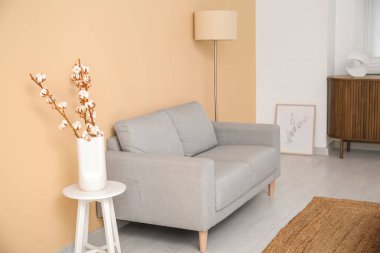 Oturma odasının içinde kanepe, lamba ve pamuklu dallar var.