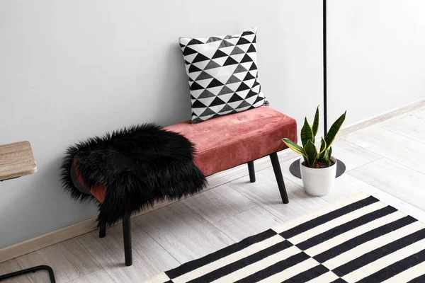 Pink bench with cushion, fur rug and houseplant near white wall