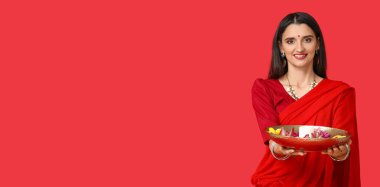 Güzel Hintli kadın elinde mum ve çiçekle kırmızı arka planda metin için yeri olan tabağı tutuyor.