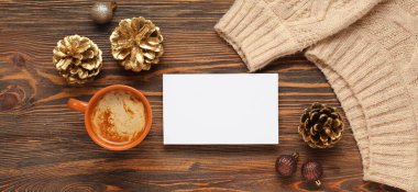 Güzel bir Noel kompozisyonu, boş tebrik kartı, kışlık süveter, dekor ve ahşap arka planda bir fincan kahve.