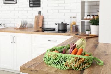 Mutfaktaki tezgahın üzerinde farklı taze sebzeler olan ağ torbası.