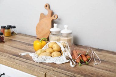 Mutfaktaki tezgahta farklı taze sebzelerle örgü torbaları var.