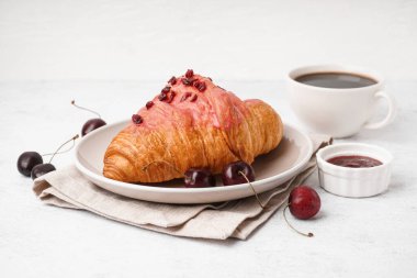 Tatlı kruvasan, kiraz ve beyaz arka planda bir fincan kahve.