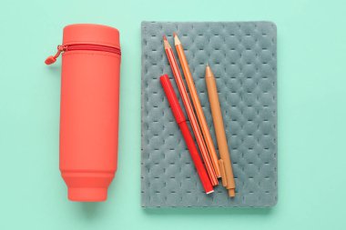 Turkuaz arka plan üzerine kalem, kalem ve defter içeren bir kutu