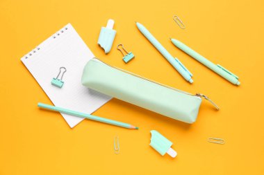 Turuncu zemin üzerinde farklı kırtasiye malzemesi ve defter bulunan kalem kutusu