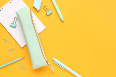 Turuncu zemin üzerinde farklı kırtasiye malzemesi ve defter bulunan kalem kutusu