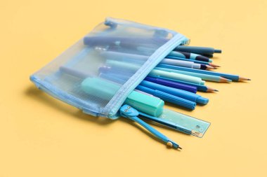 Bej arka planda okul kırtasiyesi olan mavi kalem çantası, yakın plan.