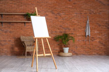 Kahverengi tuğla duvarın yanında boş tuval olan ahşap sehpa