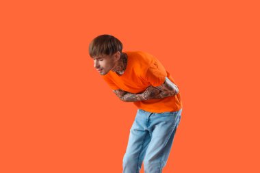 Turuncu arka planda karın ağrısı çeken genç bir adam.