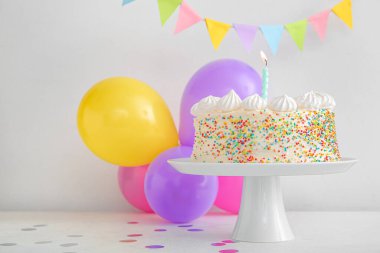 Lezzetli pasta ve doğum günü süslemeleriyle duvara yakın beyaz masada dur.