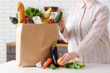 Mutfaktaki masada farklı ürünleri olan kadın ve kese kağıdı.