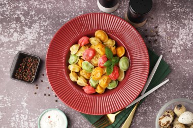 Bir tabak kaynamış renkli hamur köftesi, fesleğen ve bir kase ekşi krema.