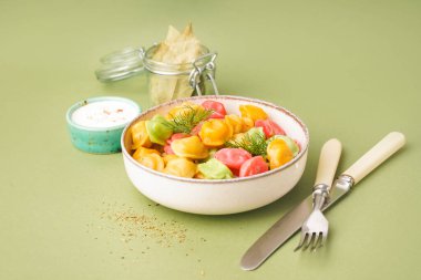 Yeşil arka planda dereotu ve ekşi kremalı bir kase kaynamış renkli börek.