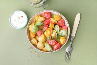 Yeşil arka planda dereotu ve ekşi kremalı bir kase kaynamış renkli börek.