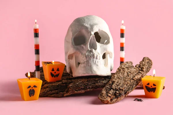 Composition with different burning candles, skull and tree barks for Halloween celebration on pink background