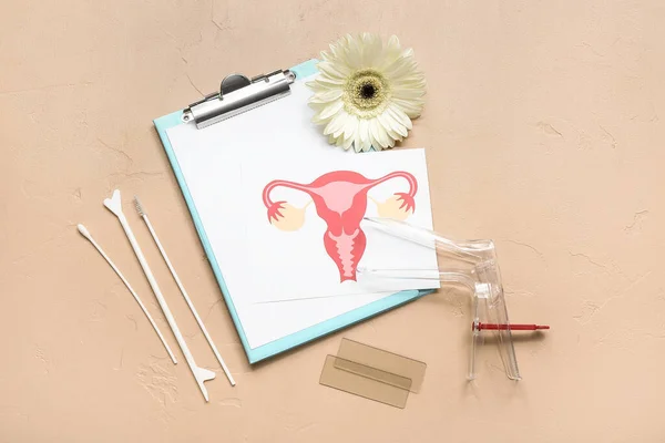 Gynecological speculum, drawing of female uterus, clipboard and pap smear test tools on beige background