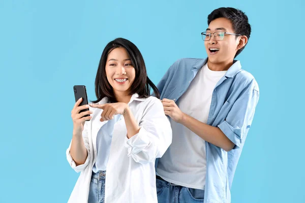 Young Asian friends with mobile phone on blue background