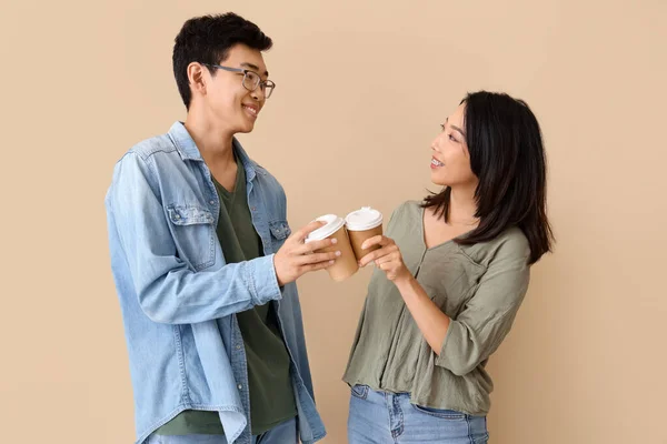 Young Asian friends with cups of coffee on beige background