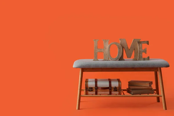 Soft bench with decor, books and suitcase on orange background